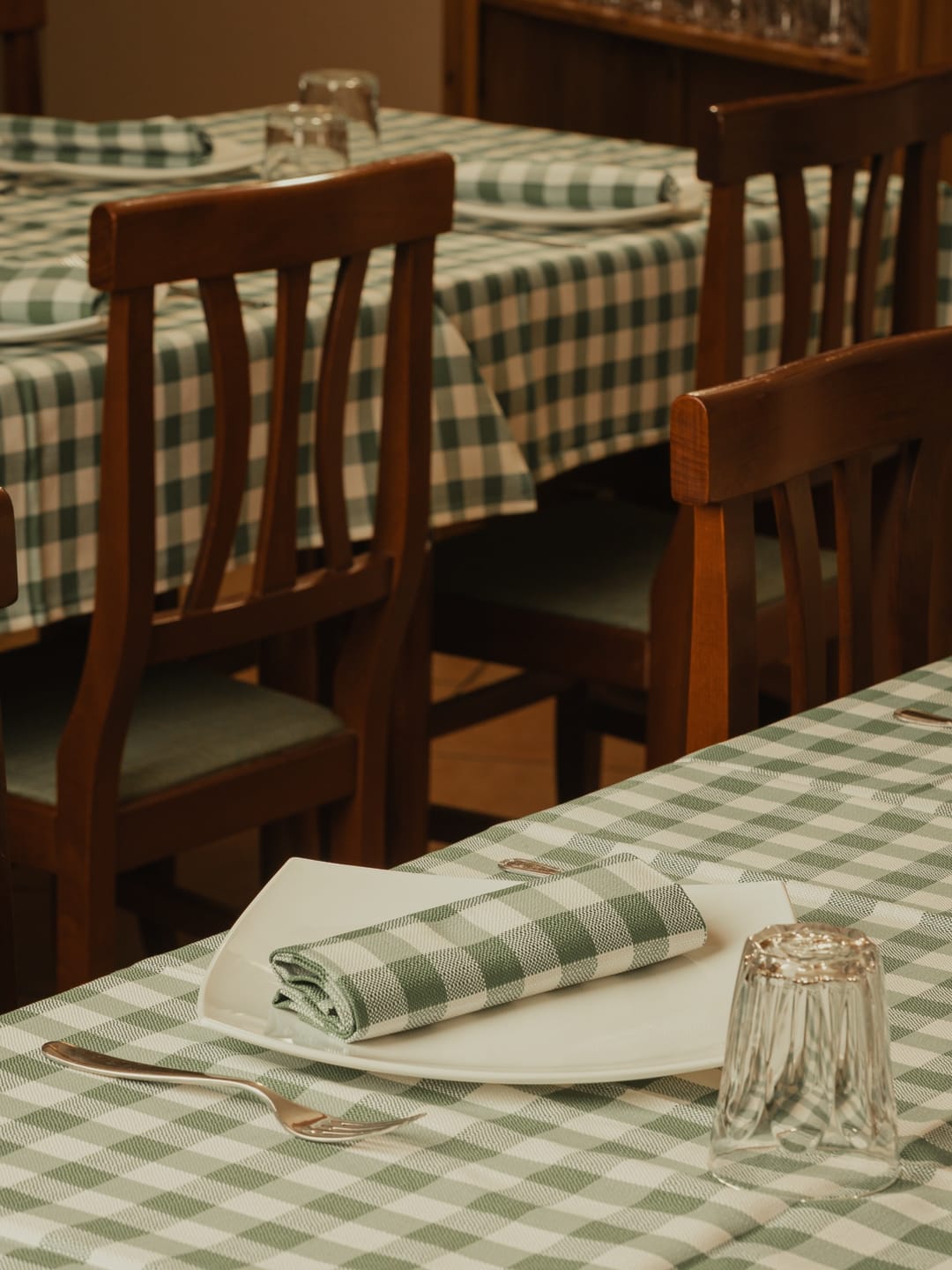 La sala della piola: tavoli apparecchiati con tovaglie a quadri verdi, tovaglioli piegati e sedie in legno.